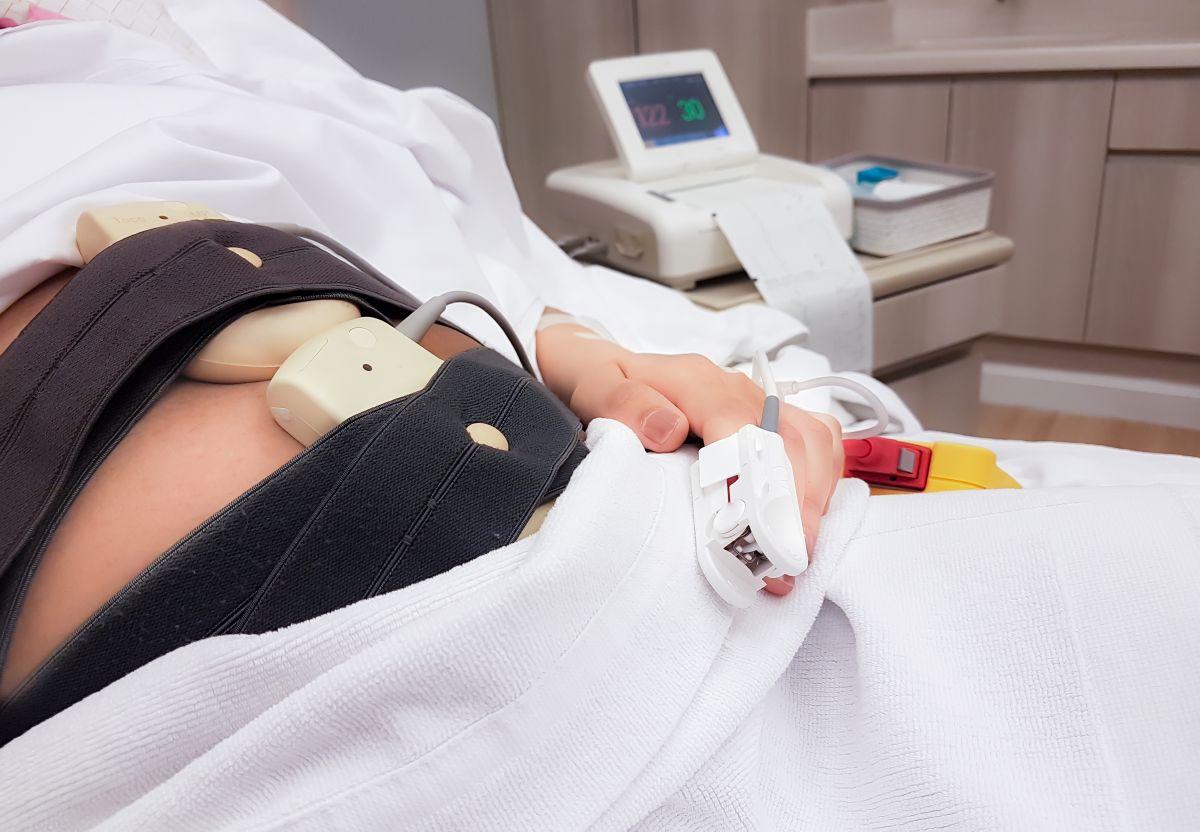 Femeie însărcinată, care stă pe un pat, la spital și are niște centuri atașate pe burtă pentru a i se face testul fetal non-stres
