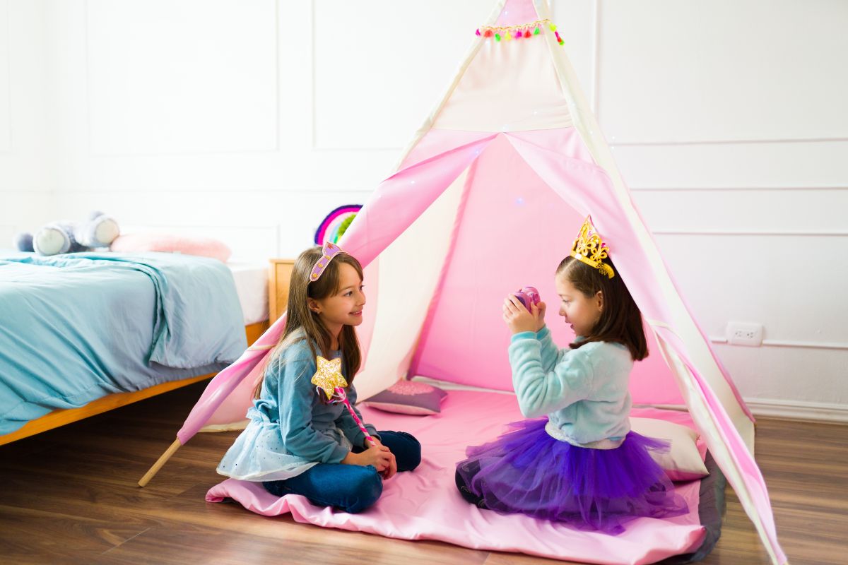 2 fetițe, îmbrăcate în prințese, cu coronițe pe cap, stau într-o cameră de copii, într-un cort roz și se joacă, ilustrând întâlnirile de joacă pentru copiii mai mari