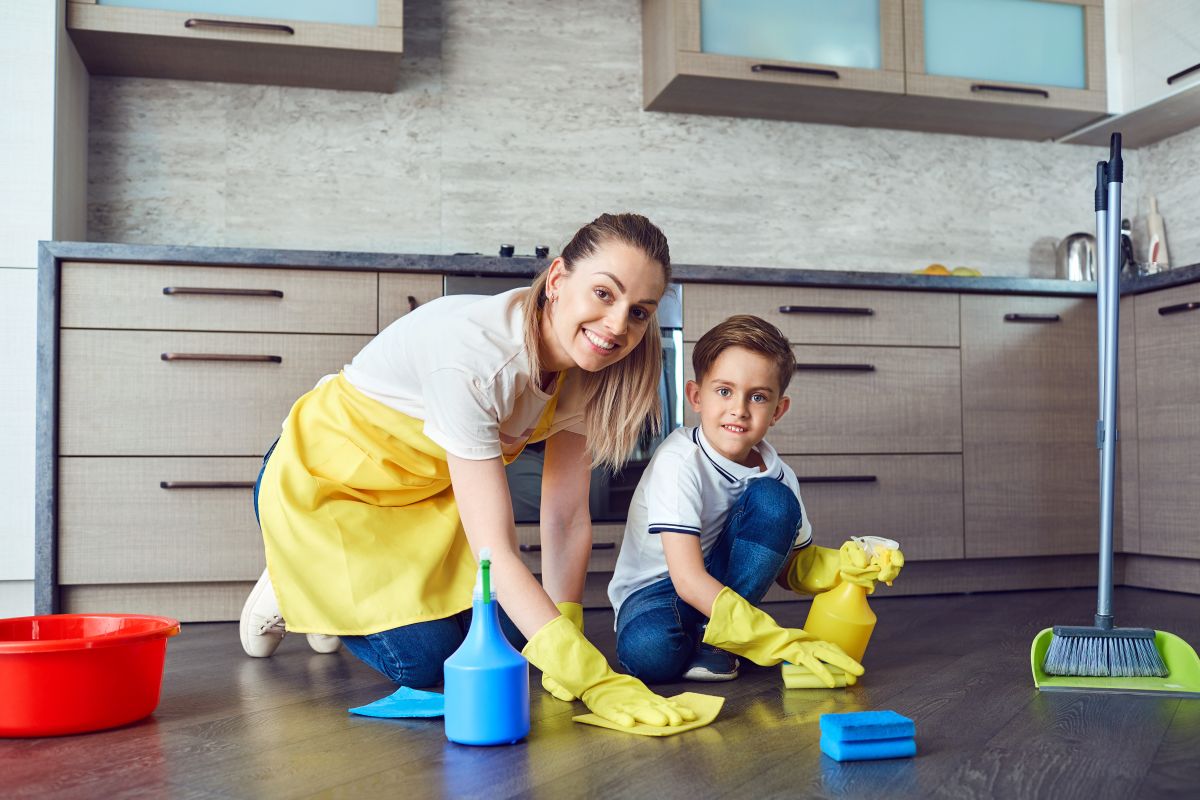 Mamă și fiu, care au mănuși galbene și curăță podeaua din bucătărie, ilustrând secretul de a crește copii fericiți și de succes