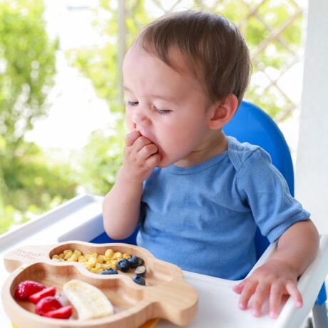 Băiat care mănâncă fructe, în scaunul de masă