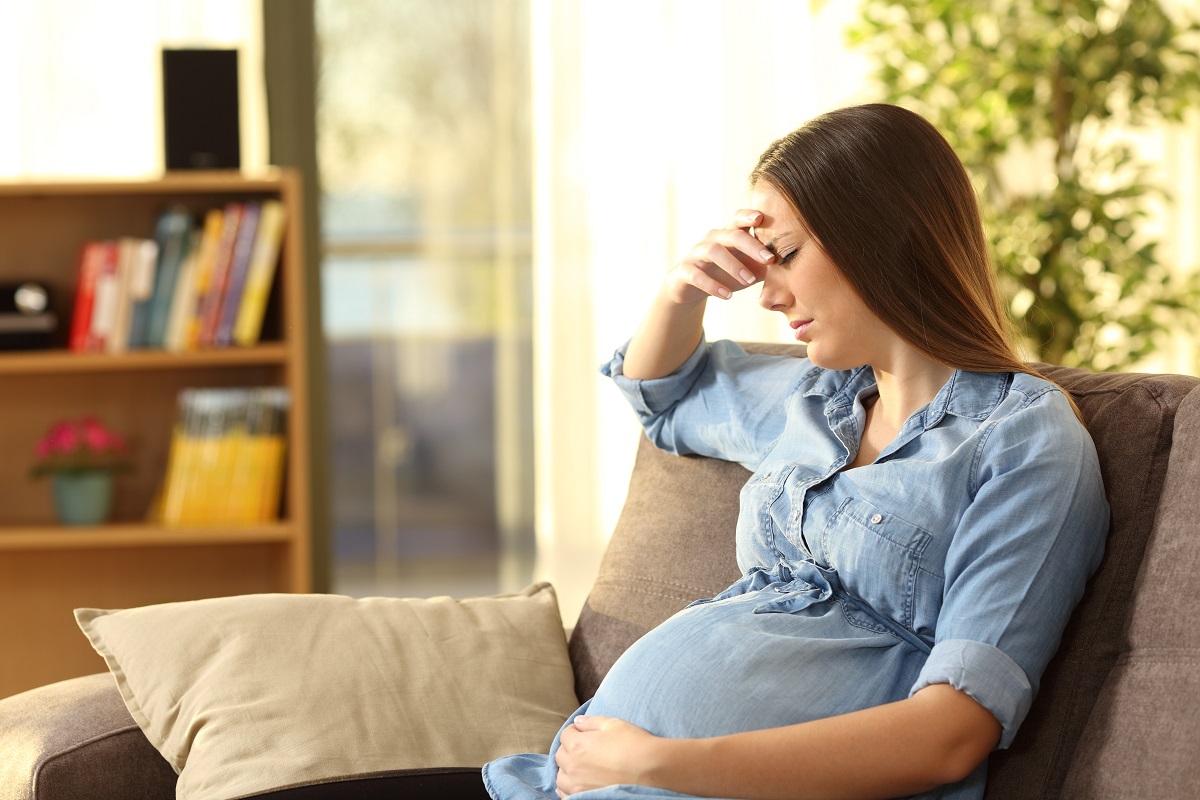 Femeie gravidă stă îngrijorată pe canapea