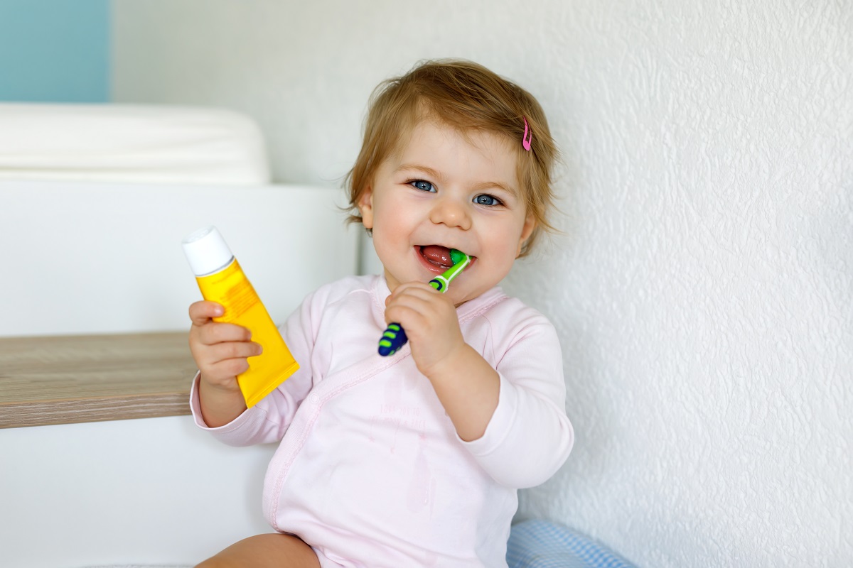 Fetiță care ține în mână o pastă și o perie de dinți