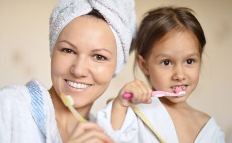 O mamă și fiica ei, în halate de baie albe care se spală pe dinți în baie