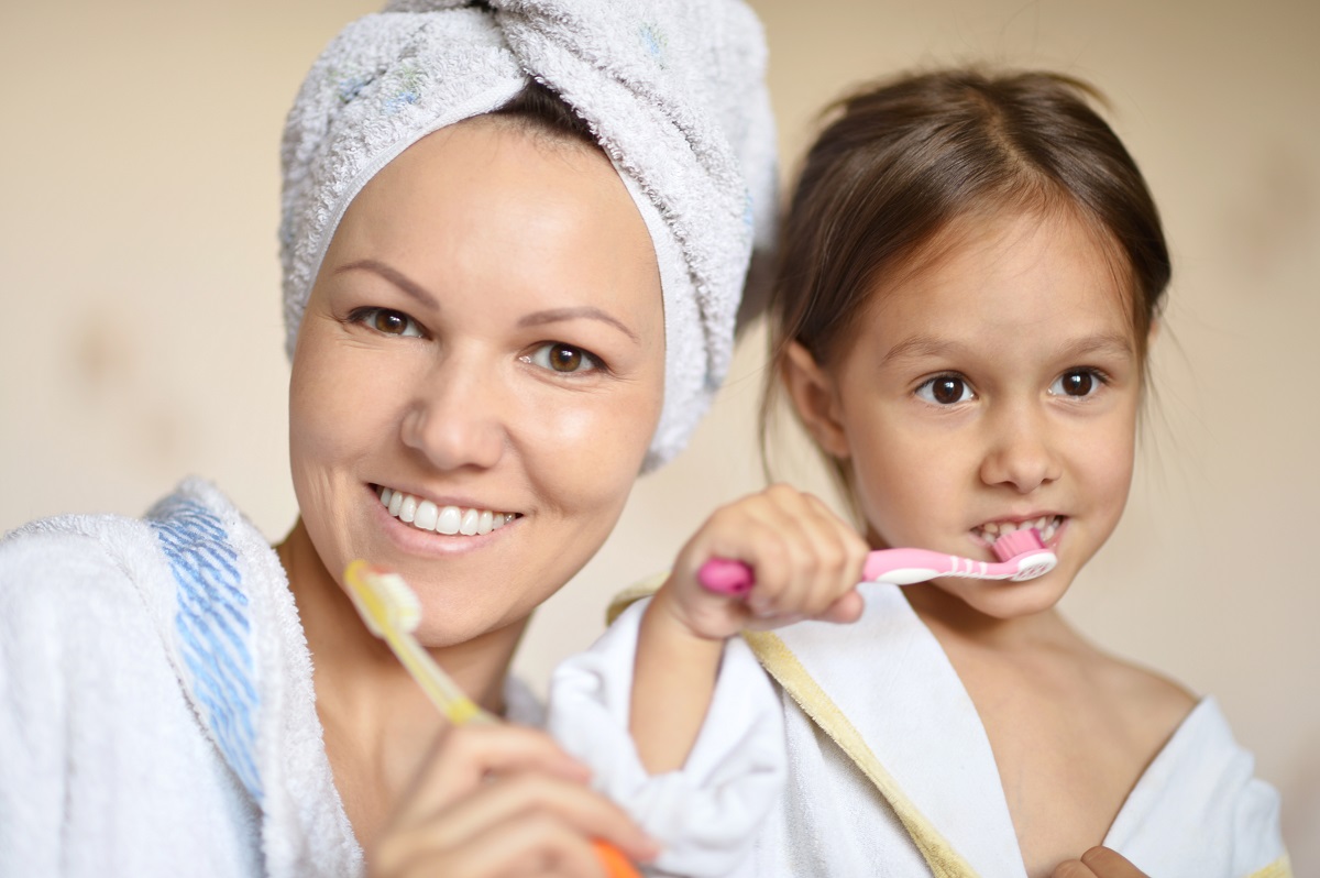 O mamă și fiica ei, în halate de baie albe care se spală pe dinți în baie