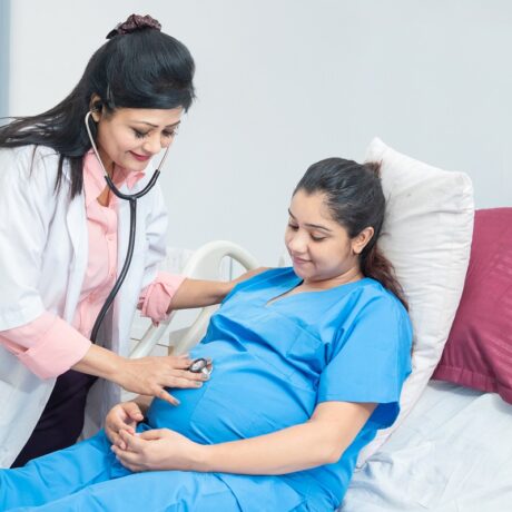 O femeie medic care consultă o pacientă însărcinată, pe un pat de spital