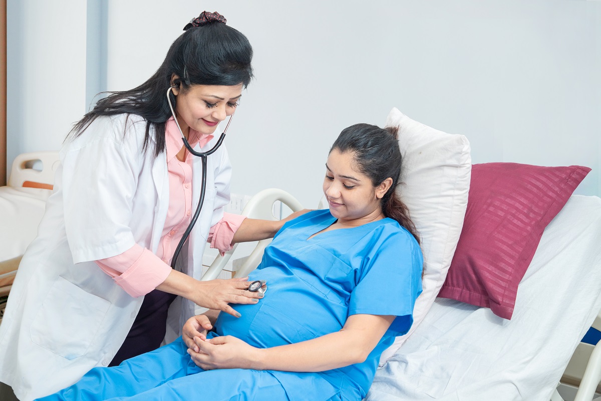 O femeie medic care consultă o pacientă însărcinată, pe un pat de spital