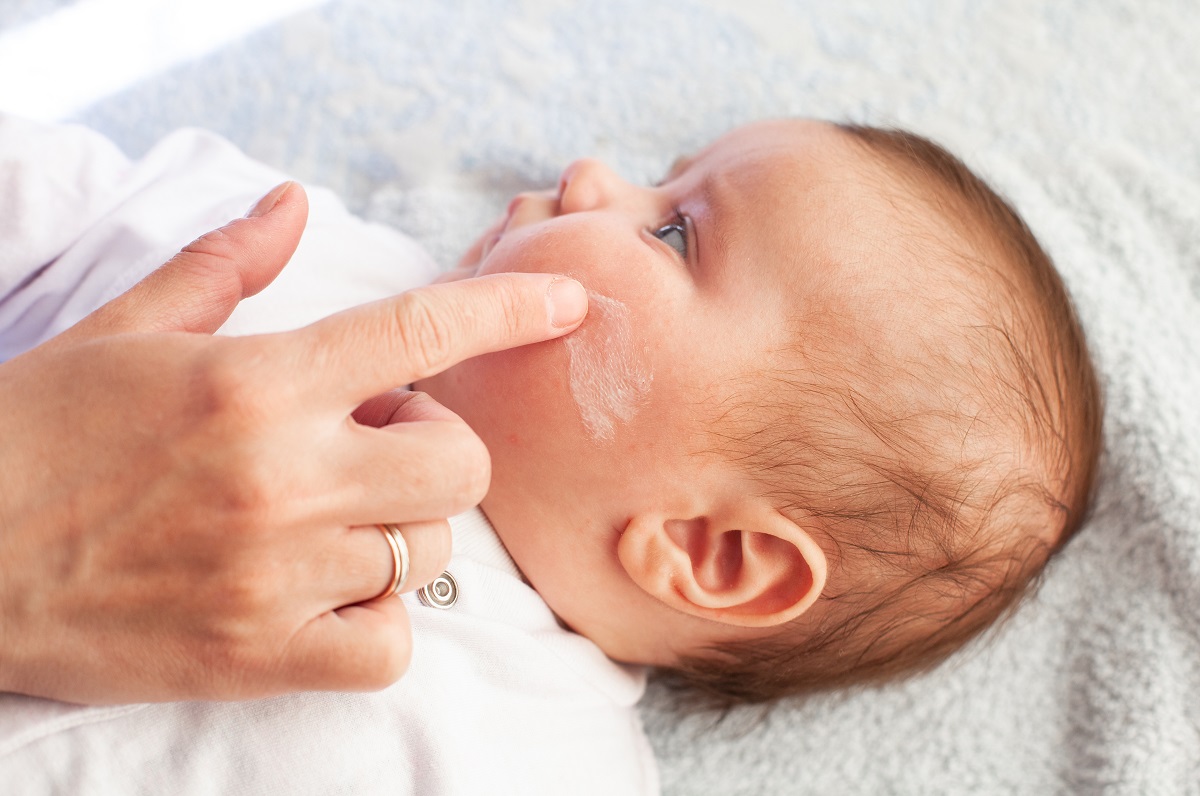 Mama îl dă pe bebeluș cu cremă pe față pentru dermatită atopică