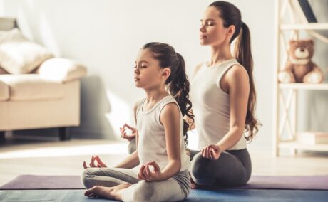 Mama și fiica ei stau pe covor și fac yoga