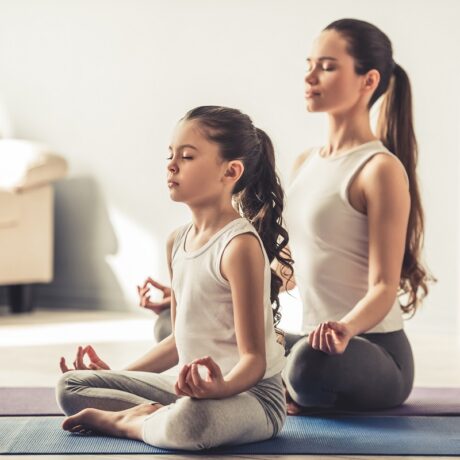 Mama și fiica ei stau pe covor și fac yoga