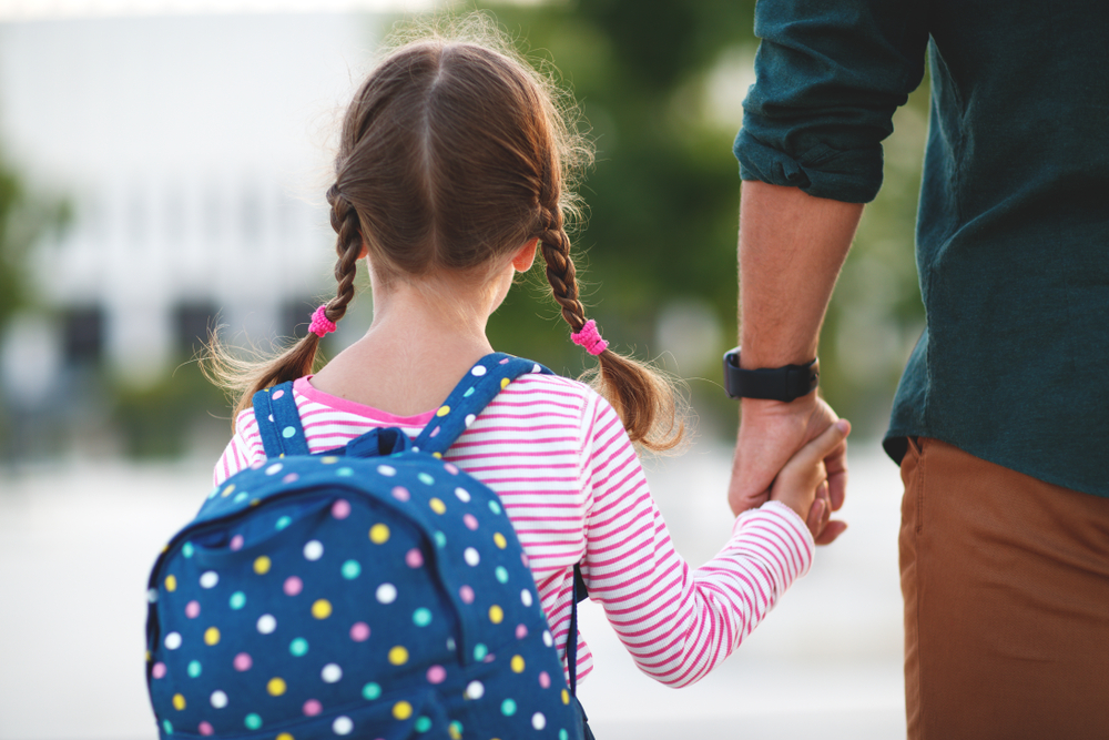 O fetiță care merge la școală de mână cu tatăl ei