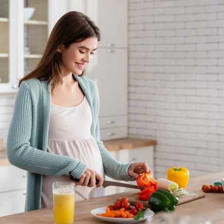Femeie gravidă taie legume în bucătărie