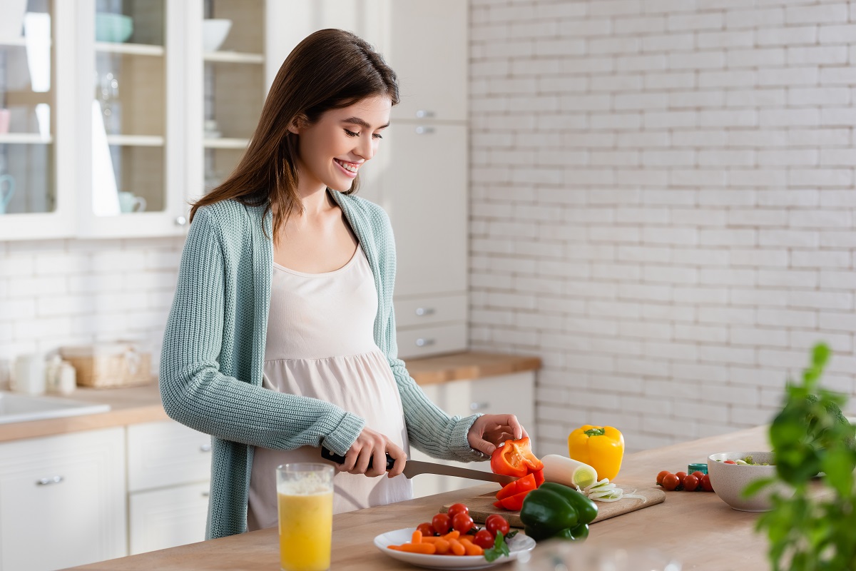 Femeie gravidă taie legume în bucătărie