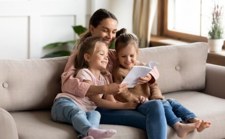 Mama stă cu fetițele pe canapea și le citește dintr-o carte