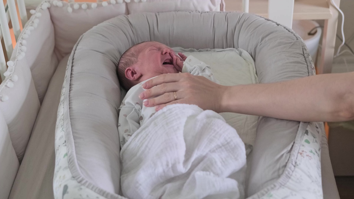 Bebeluș plânge în timp ce doarme, iar mâna mamei îl liniștește