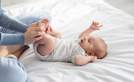 Bebeluș stă întins pe pat și face exerciții la picioare