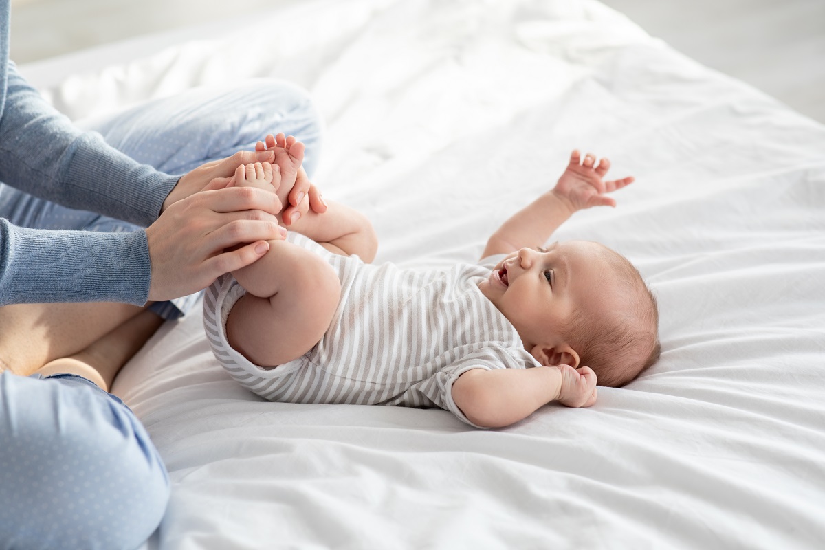 Bebeluș stă întins pe pat și face exerciții la picioare