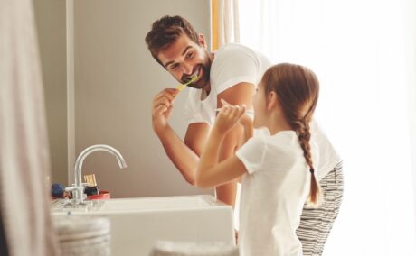 Copil care se spală pe dinți alături de tata sunt în baie cu periuțele de dinți