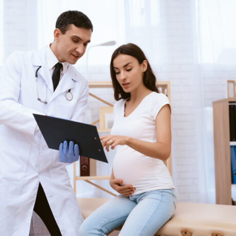 Femeie gravidă în cabinetul doctorului stă de vorbă cu el