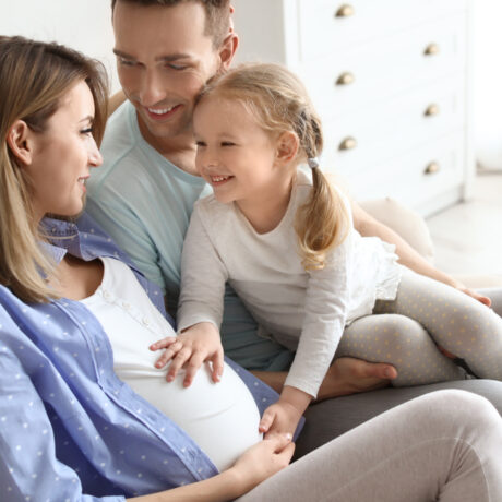 Femeie însărcinată alături de familie, zâmbește