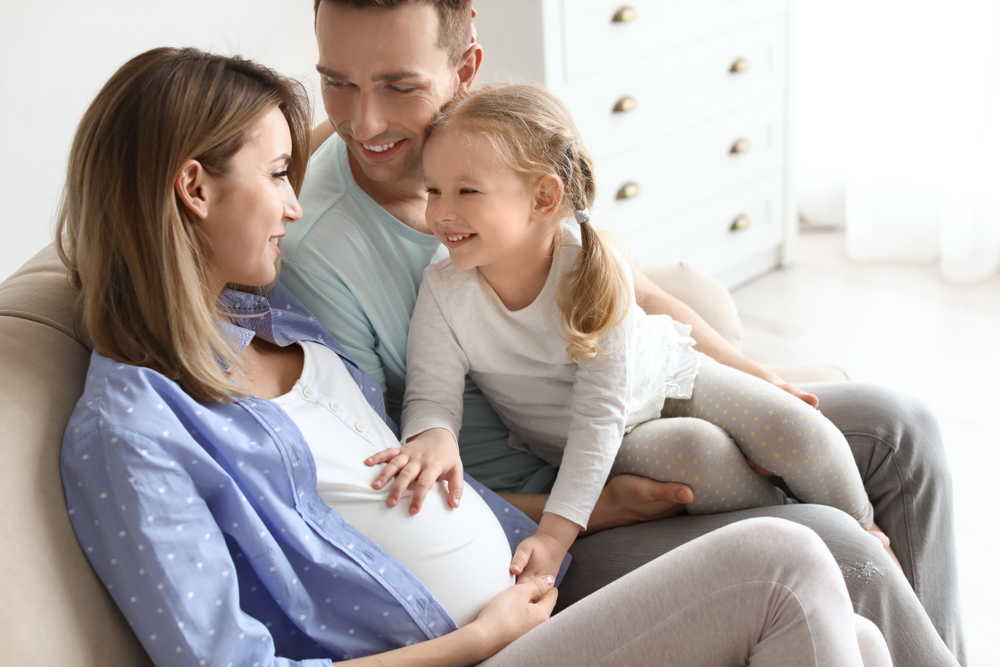 Femeie însărcinată alături de familie, zâmbește
