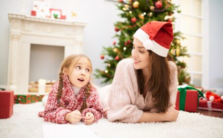 Mama cu fetița stau pe covor și vorbesc despre Moș Crăciun