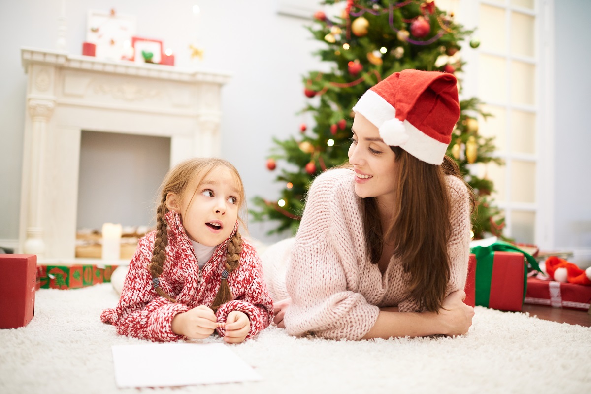 Mama cu fetița stau pe covor și vorbesc despre Moș Crăciun