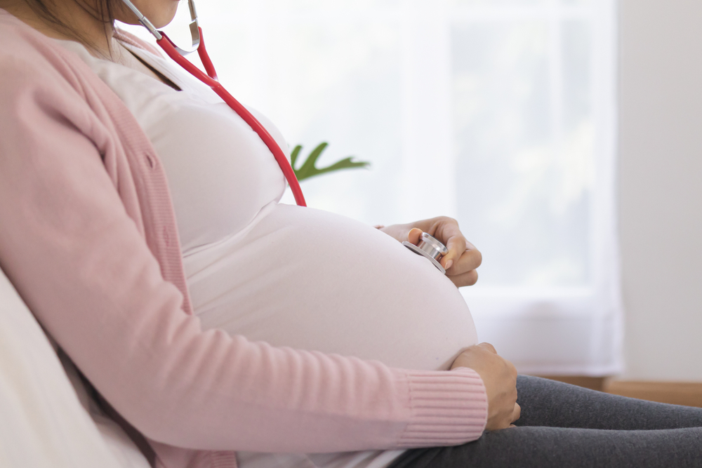 Femeie însărcinată își ține mână pe burtă și un stetoscop