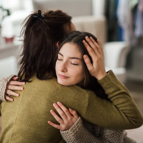 Fată tânără se îmbrățișează cu mama ei într-o casă