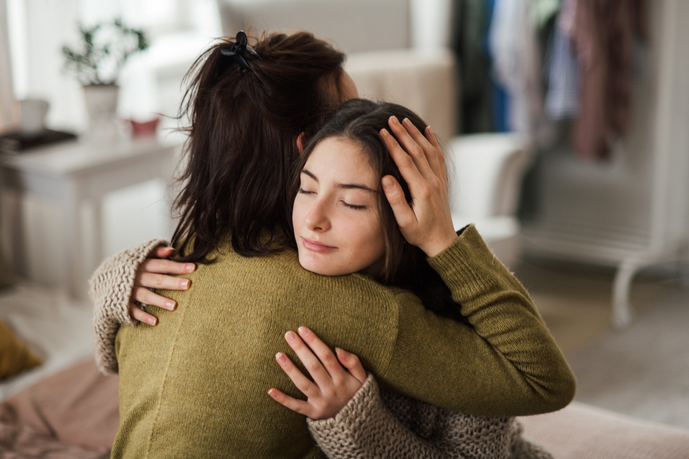 Fată tânără se îmbrățișează cu mama ei într-o casă