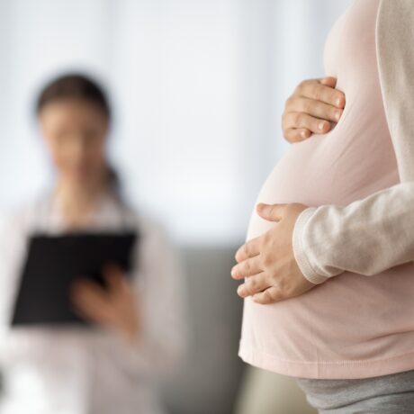 Femeie gravidă ține mâna pe burtă în cabinetul doctorului