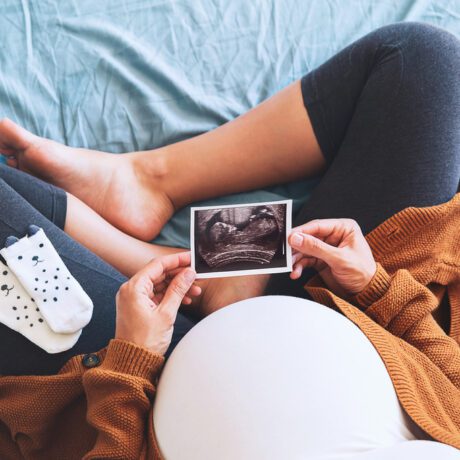 Femeie însărcinată stă în pat și se uită la ecografie cu o pereche de șosete pe picior