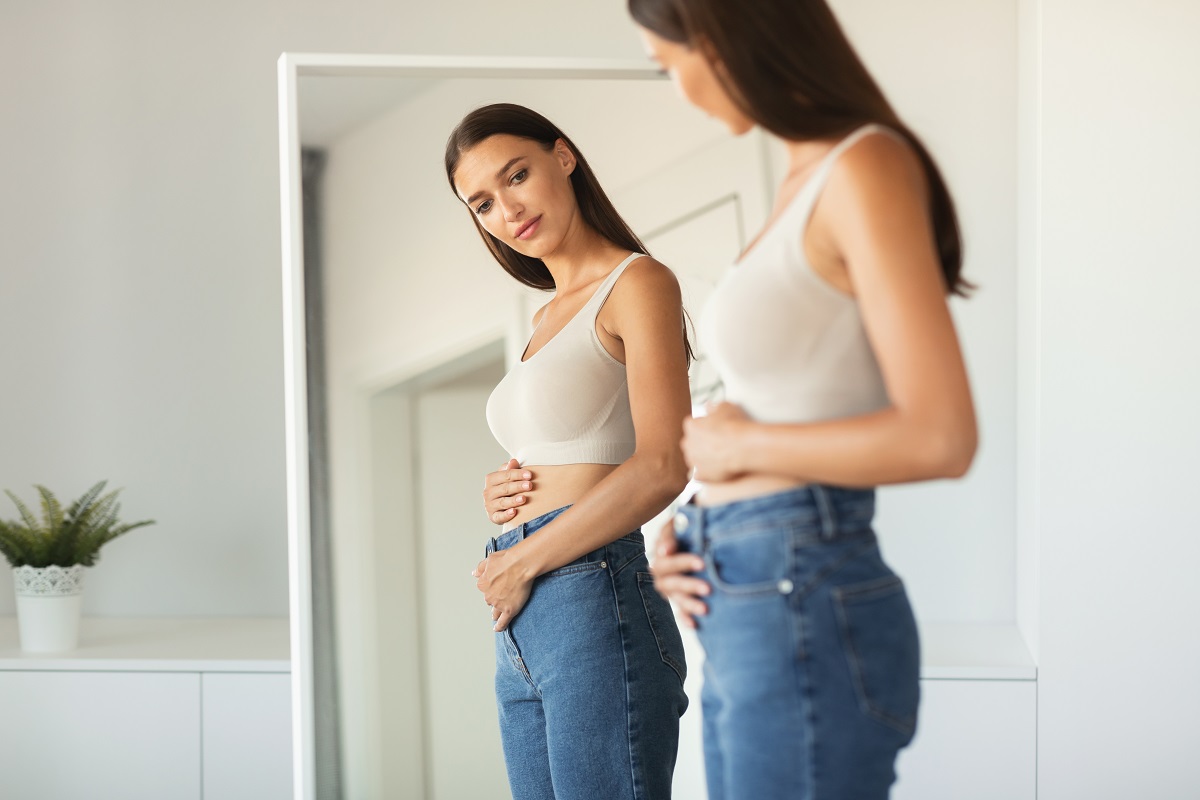 Femeie își privește corpul în oglindă