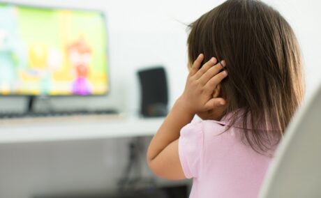Fetița își ține mâinile la urechi când se uită la televizor