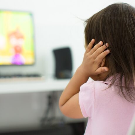 Fetița își ține mâinile la urechi când se uită la televizor