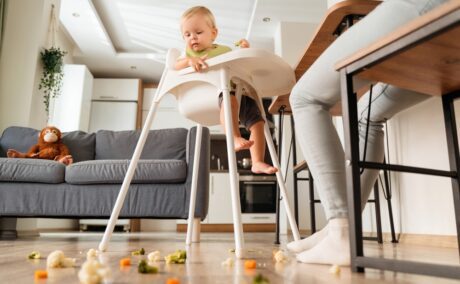 Bebeluș care stă într-un înălțător se uită la mâncarea căzută pe podea