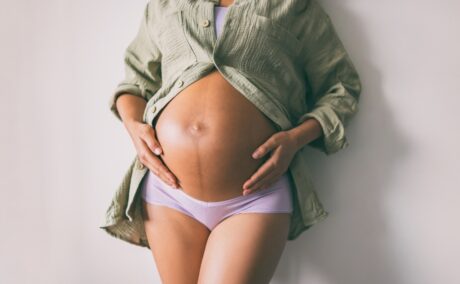 Femeie însărcinată cu burtica la vedere își ține mâinile pe burtă