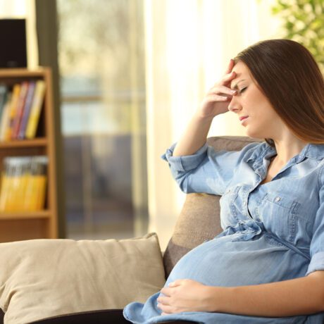 O femeie gravidă, nervoasă, care stă pe o canapea