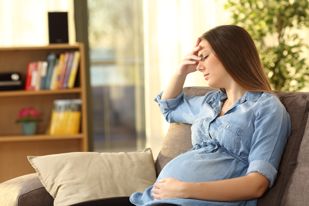 O femeie gravidă, nervoasă, care stă pe o canapea