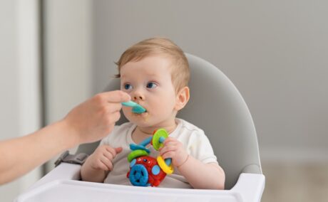 Un copil care este hrănit cu lingurița în timp ce stă într-un scaun special