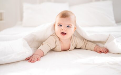 Un bebelu; care st[ pe burtic[ ]ntr-un pat alb pentru a putea ilustra cele mai populare nume de benelu;i ]n anul 2024