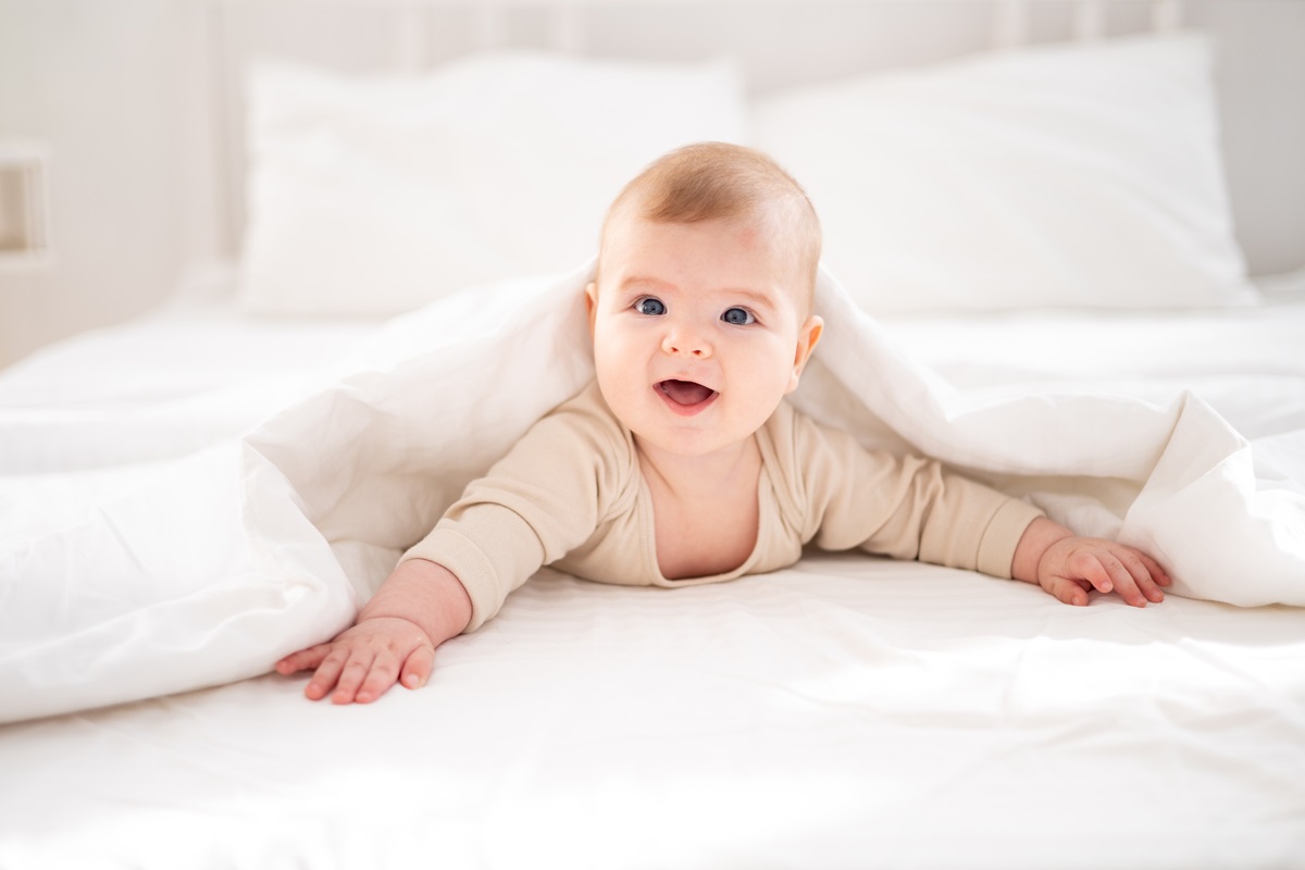Un bebelu; care st[ pe burtic[ ]ntr-un pat alb pentru a putea ilustra cele mai populare nume de benelu;i ]n anul 2024