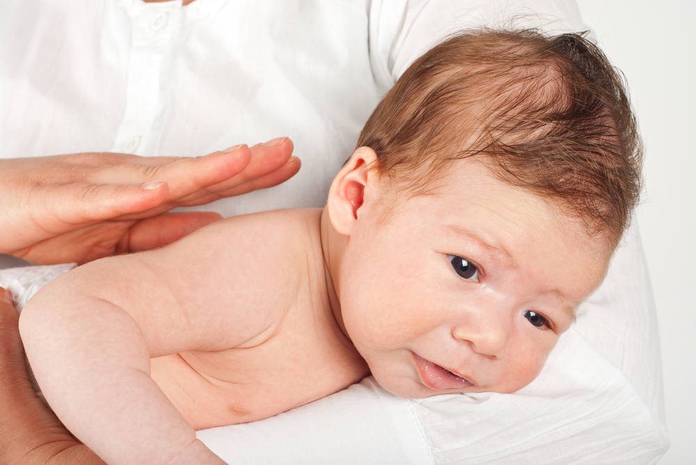 Bebeluș ținut pe burtă și mămică ce îl ajută să scoată aerul din stomac