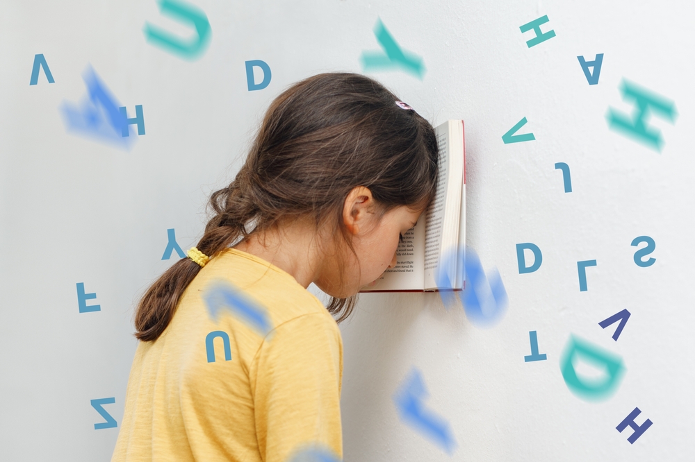 Fetiță tristă care stă cu capul pe perete în fața unei cărți cu multe litere care zboară pe lângă ea