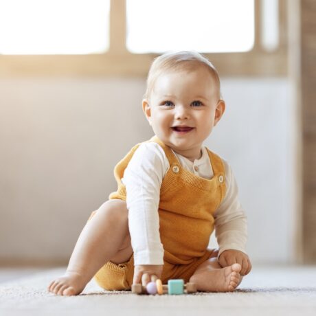 Un bebeluș fericit care stă pe un covoraș și se joacă cu cuburi colorate