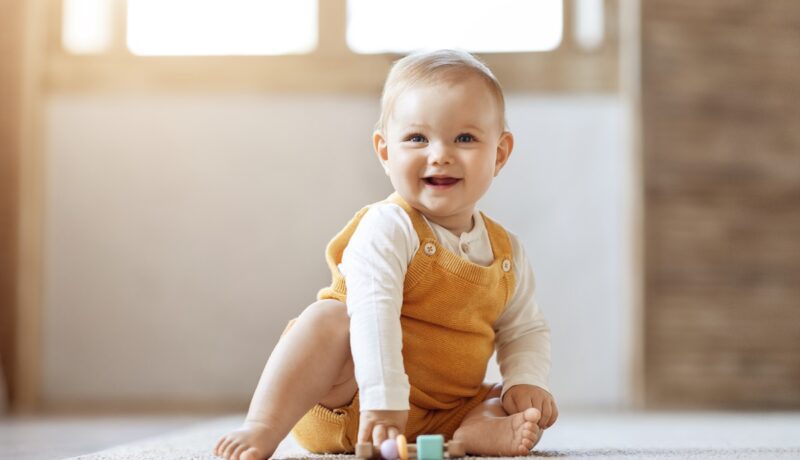 Un bebeluș fericit care stă pe un covoraș și se joacă cu cuburi colorate