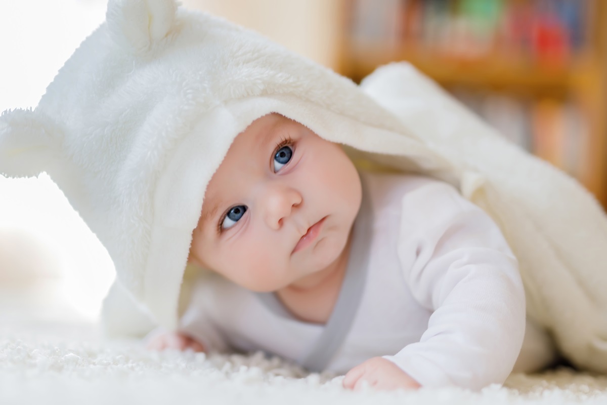 Un nou-născut care stă pe un covoraș pufos și este acoperit cu un prosop pentru a ilustra cum să ai grijă de un bebeluș în timpul iernii