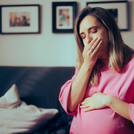 Femeie gravidă poartă o cămașă roz și are grețuri