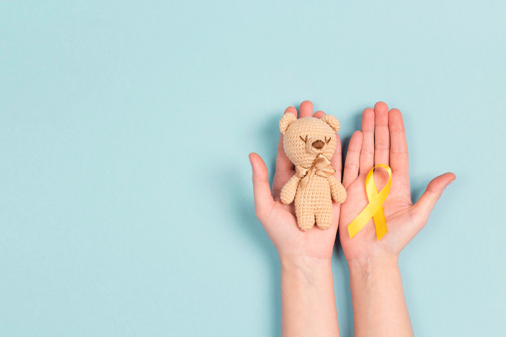 Un copil care ține în mână o jucărie din pluș și o fundiță galbenă