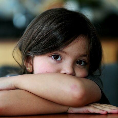 Fetiță privește tristă cu capul pe brațe