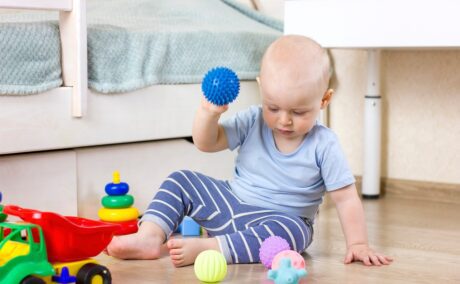 Băiețelul se joacă pe podea cu câteva mingi
